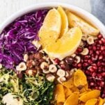 A close up look at a salad bowl filled with red cabbage, oranges, pomegranate, butternut squash, and hazelnuts.