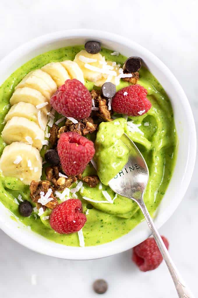 A vegan green smoothie shown topped with bananas, raspberries and granola.