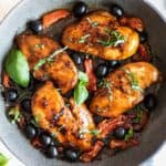 Balsamic chicken breasts in a pan with sundried tomatoes, olives and basil.