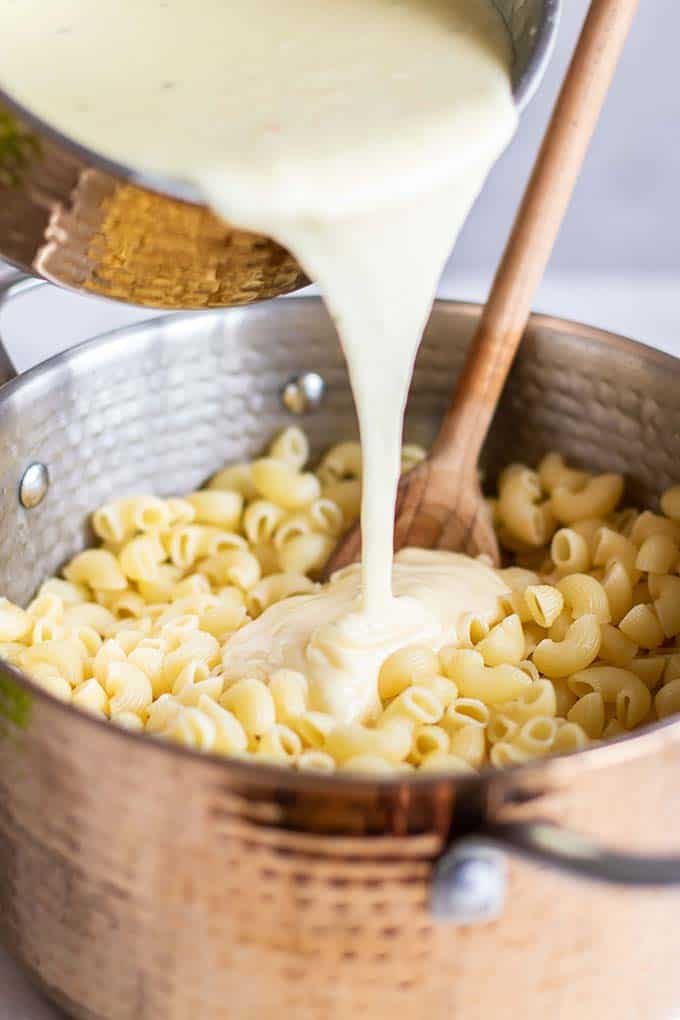 A white cheddar cheese sauce being poured onto a pan of macaroni noodles.