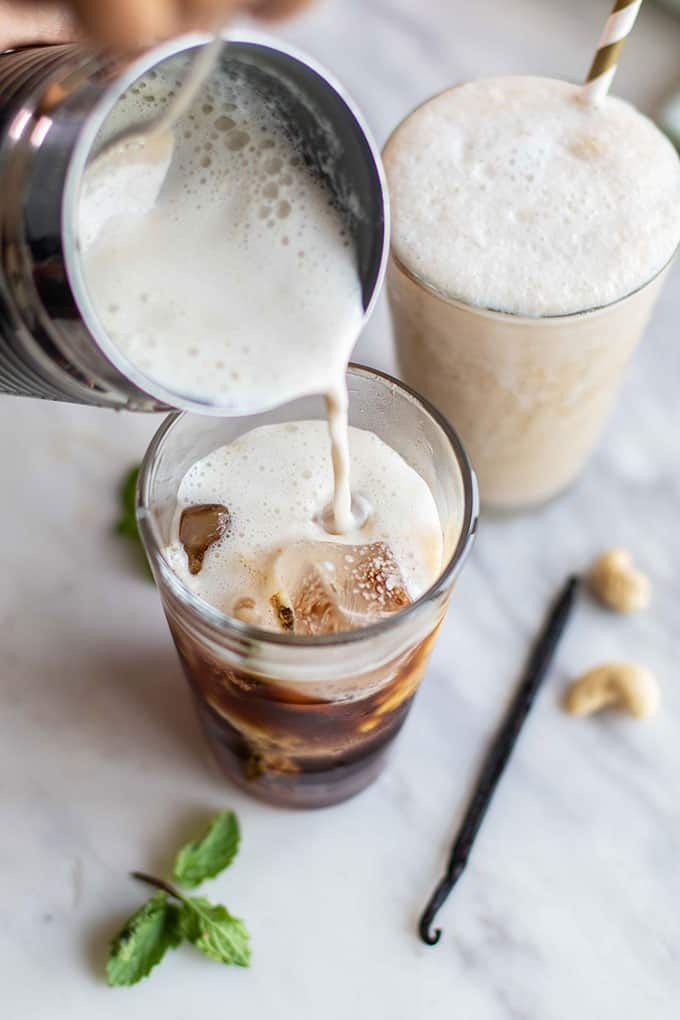 Pouring vanilla cashew milk into an iced coffee.