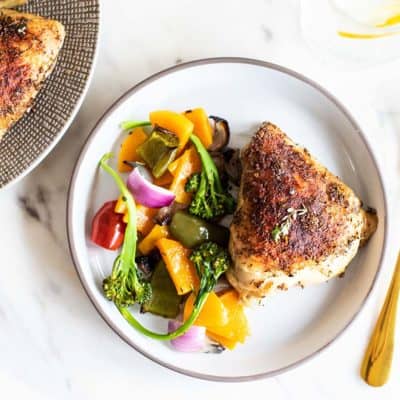 A plate with a baked chicken thigh and a serving of roasted vegetables.