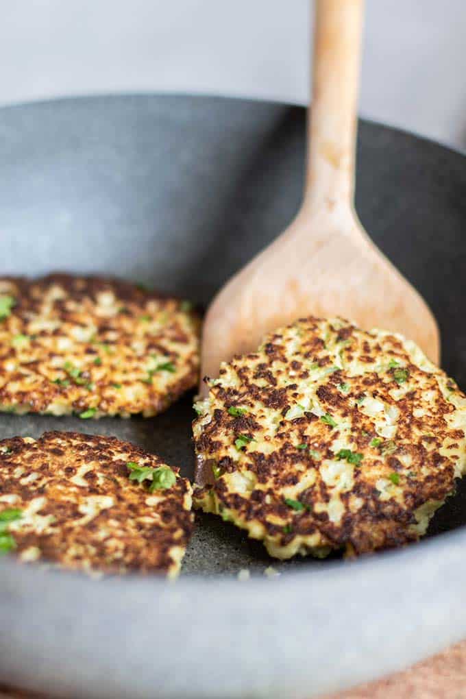 Crispy cauliflower fritters being fried in a skillet.