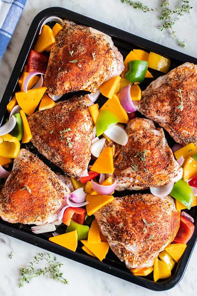 Seasoned chicken thighs on a sheet pan with lots of colorful veggies.