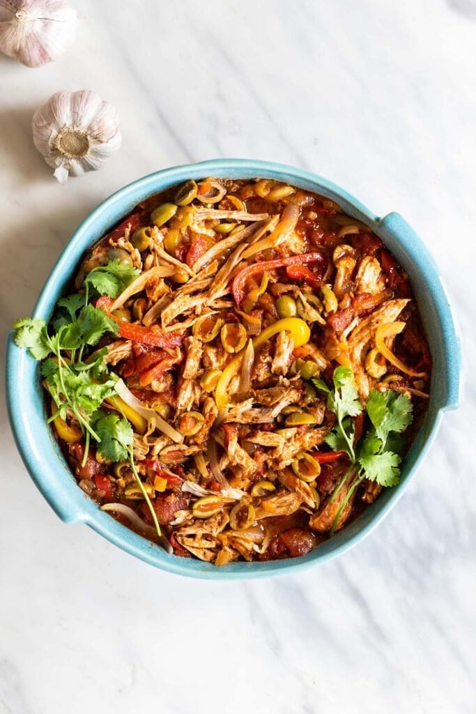 A blue casserole dish filled with shredded pork, tomatoes, peppers, and onions.