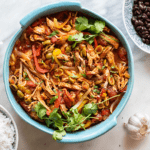 A blue baking dish filled with shredded pork, onions, peppers, and olives, a dish called Ropa Vieja.