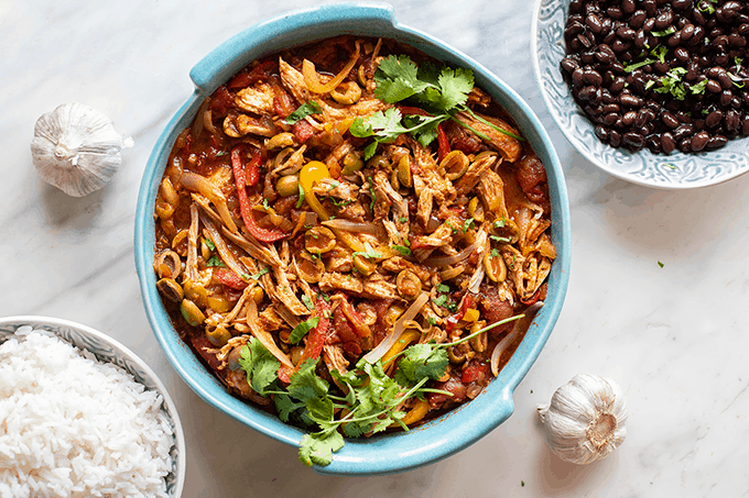 A blue baking dish filled with shredded pork, onions, peppers, and olives, a dish called Ropa Vieja.