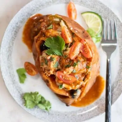 An enchilada stuffed sweet potato topped with tomatoes and cilantro.