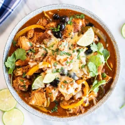 A dish showing crockpot enchilada chicken garnished with limes, cheese, and cilantro.