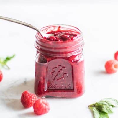 A jar of raspberry chia jam with a spoon scooping some out.