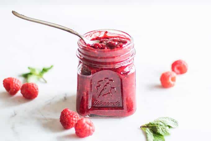 A jar of chia seed jam with raspberries and mint leaves.