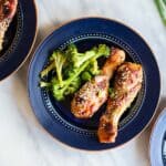 Oven baked chicken legs served on a blue plate with broccoli.
