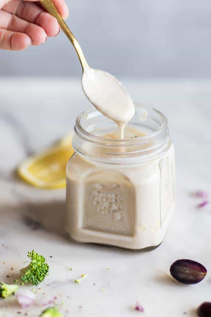 A spoon drizzling a creamy tahini dressing in a jar.