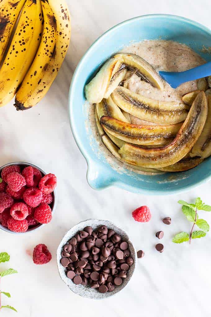 A bowl of banana bread batter with caramelized bananas, showing raspberries and chocolate chips as optional add-ins.