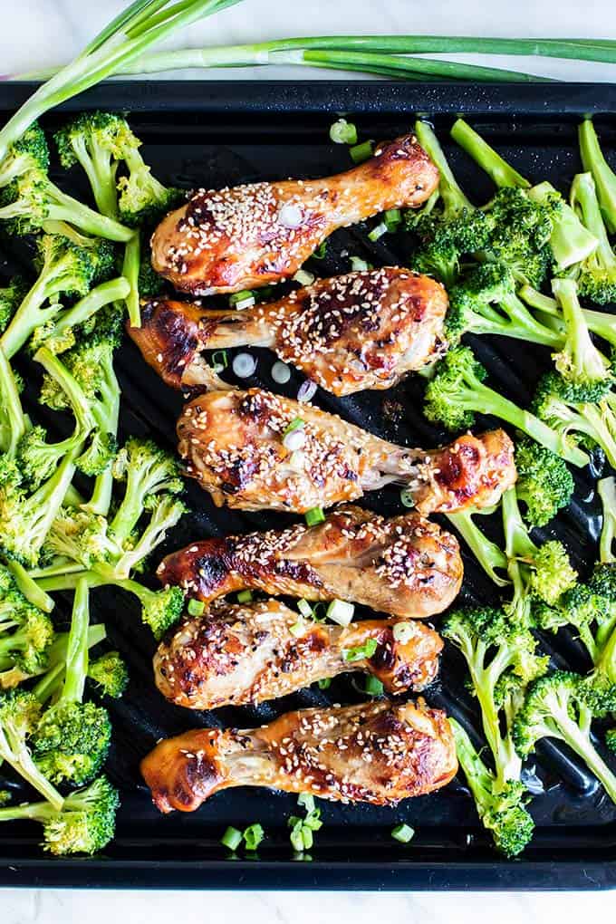 Oven baked chicken legs shown sprinkled with sesame seeds between roasted broccoli.