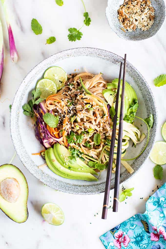 A Thai noodles dish with chop sticks, garnished with avocado and herbs.