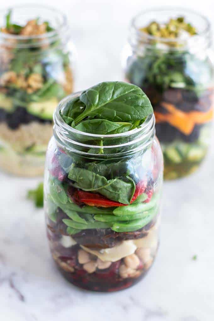 A 3 bean mason jar salad packed, sitting in front of two other mason jar salads.