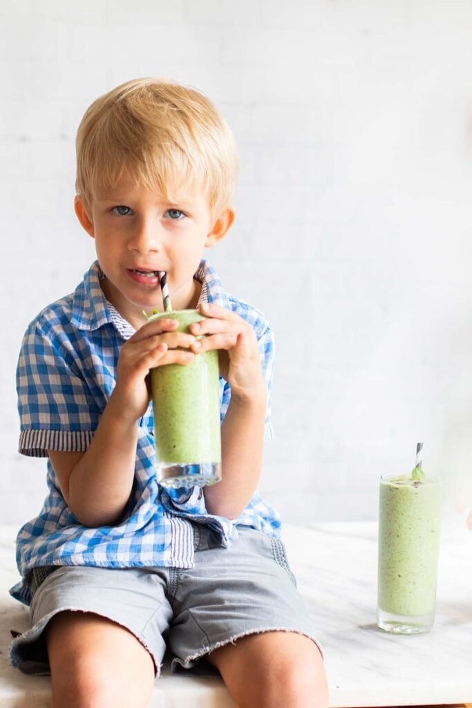 A toddler enjoying a green smoothie.