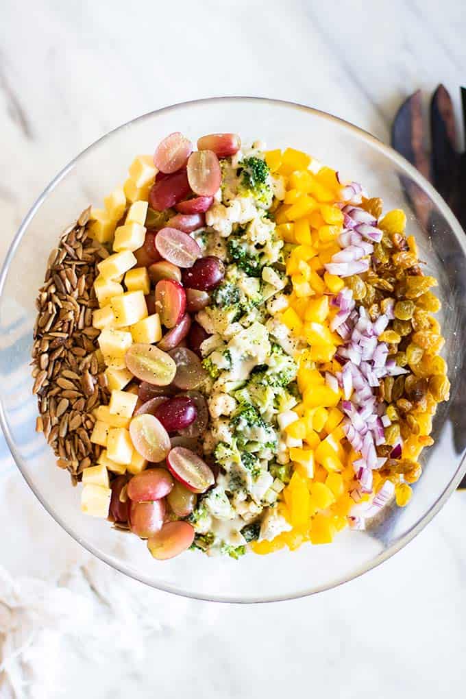 A top down view of a broccoli and cauliflower salad with rows of colorful toppings.