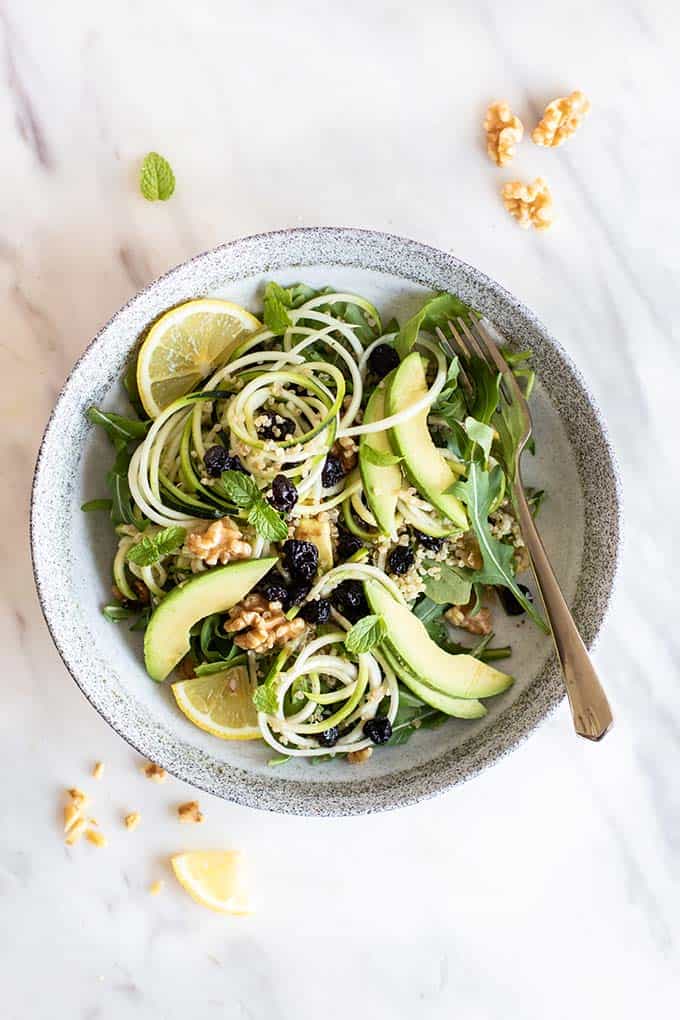 A cherry quinoa zoodle salad tossed in a creamy tahini dressing on a white plate.