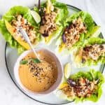A white plate with chicken lettuce wraps and a bowl of Thai dipping sauce.