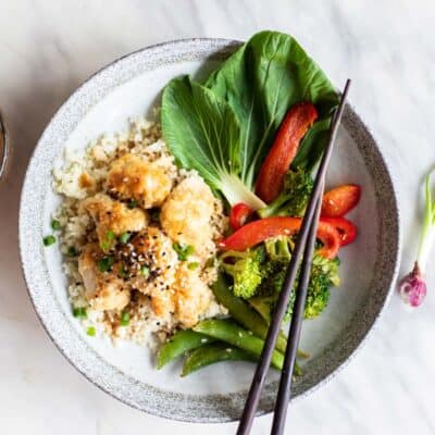 A white plate with cauliflower rice, gluten free sweet and sour chicken, and baked vegetables.