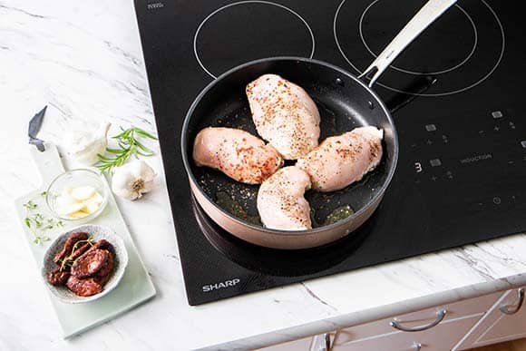 4 chicken breasts shown browning in a skillet on an induction cooktop.