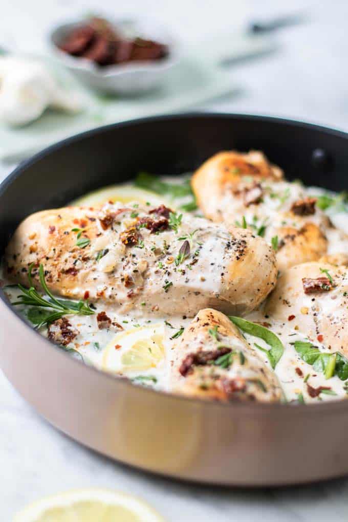 A side view of a chicken breast covered in whole30 cream sauce and garnished with herbs.
