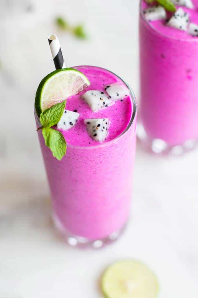 A beautiful bright pink dragon fruit smoothie in a glass, garnished with mint, lime, and white dragon fruit,