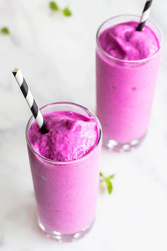 Two clear glasses with black paper straws, filled with a thicky and creamy dragon fruit smoothie.