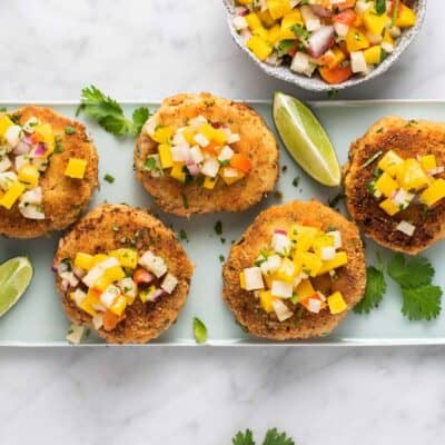 A blue plate with zucchini salmon patties topped with mango salsa.