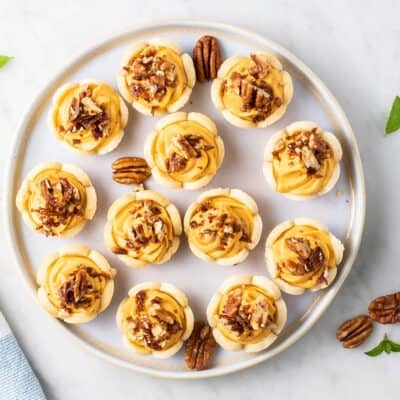 A top view of a plate of mini pumpkin pies topped with pecans.
