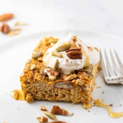 A piece of pumpkin pie baked oatmeal on a plate topped with whipped cream and honey.