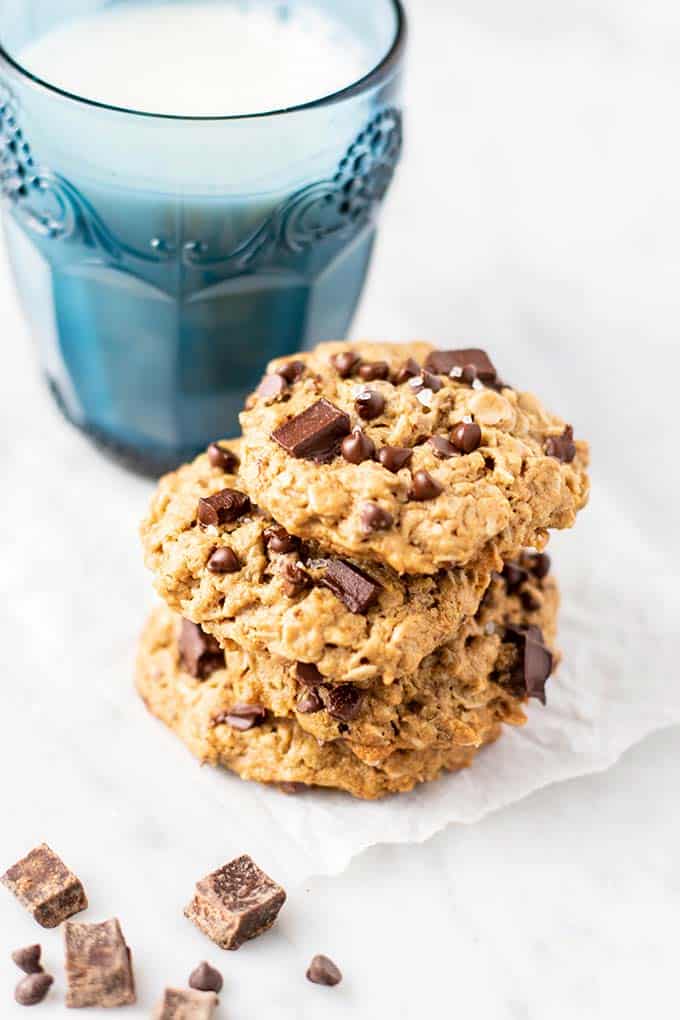 Three vegan oatmeal cookies in front of a glass of milk.