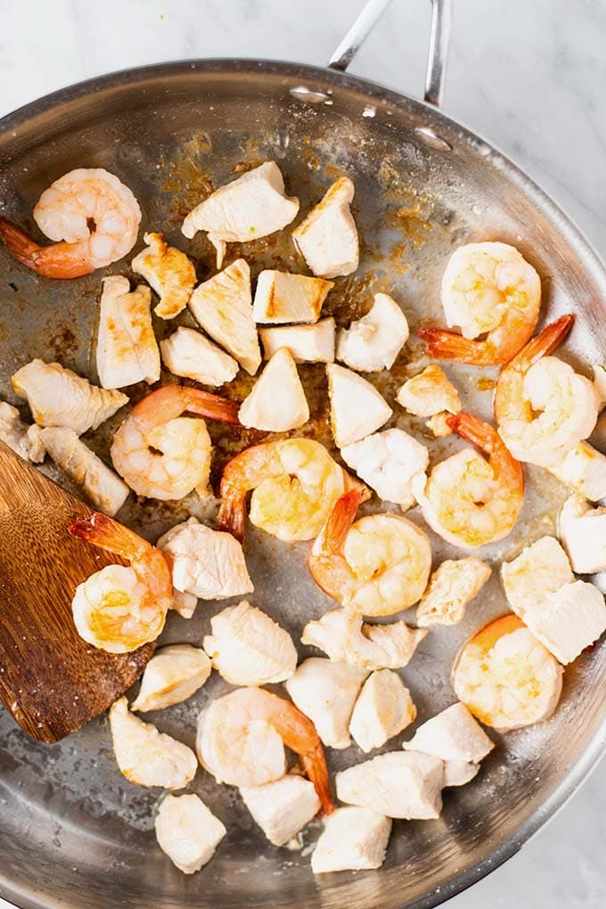 Chicken and shrimp browning in a skillet.