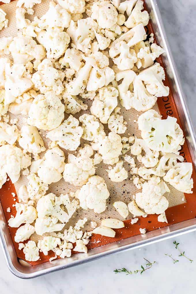 Raw cauliflower and garlic cloves on a baking tray.