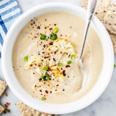 A bowl of creamy cauliflower soup topped with green onions and red chili flakes.