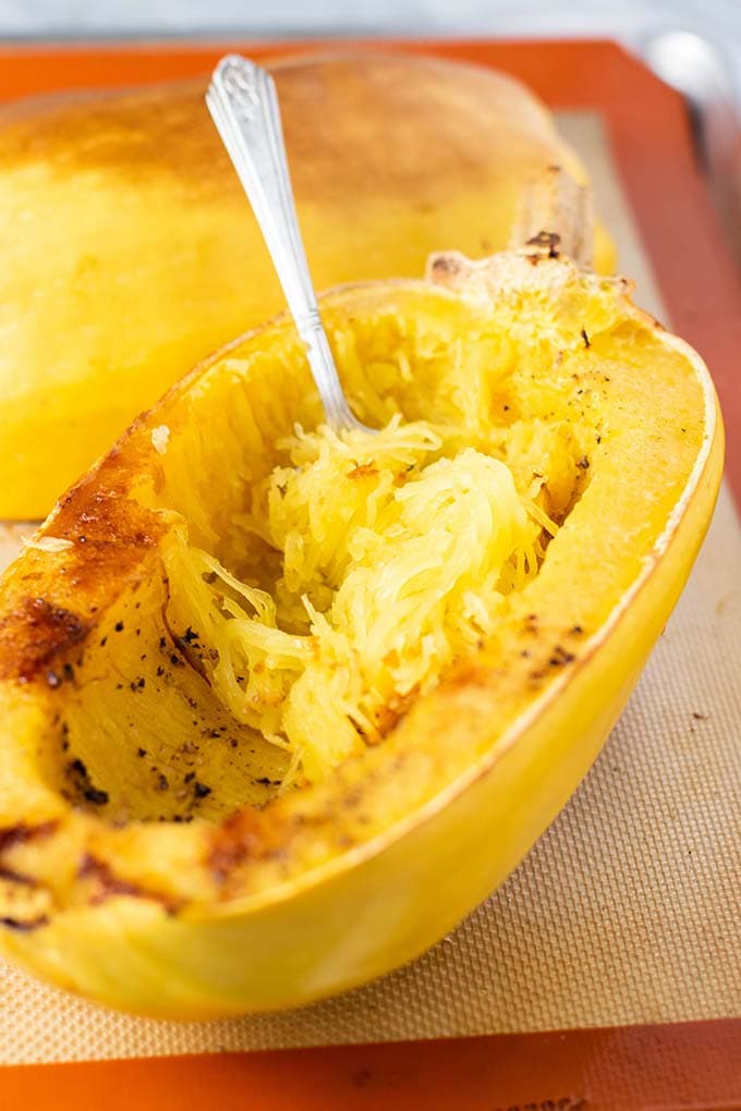 A baked and browned spaghetti squash with a fork pulling strands from the inside.