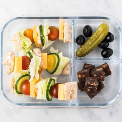 A lunch box with cheese sandwich skewers, pickles, and fruit.