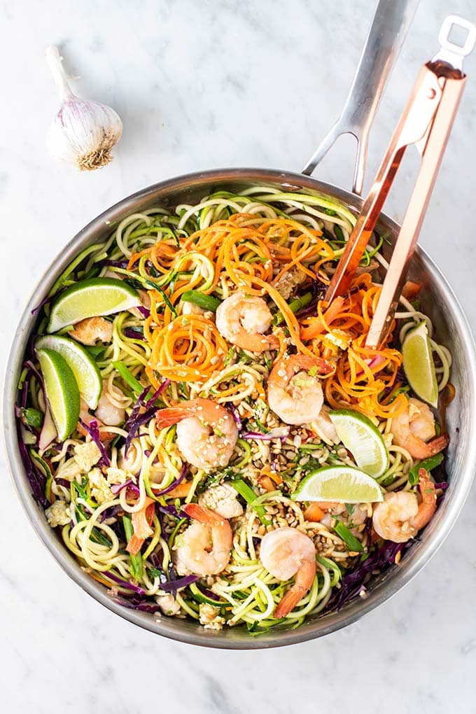 A large skillet filled with zucchini, carrot noodles, purple cabbage, chicken and shrimp.