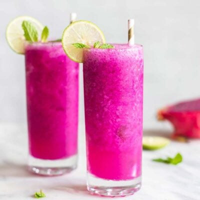 Two mango dragon fruit refreshers in tall glasses garnished with lime.