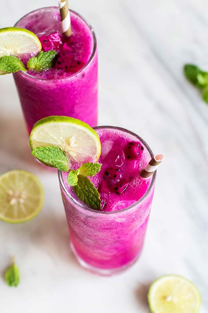 Two mango dragon fruit refreshers with lime slices and mint leaves.