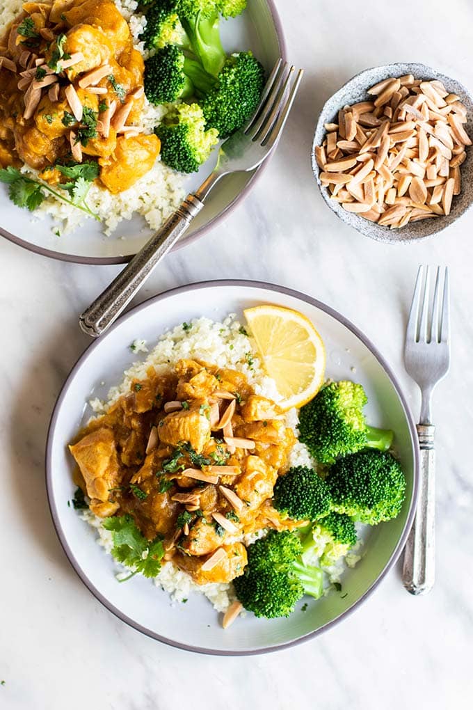 Two plates with cauliflower rice, broccoli, and crockpot pumpkin chicken, topped with toasted almonds.