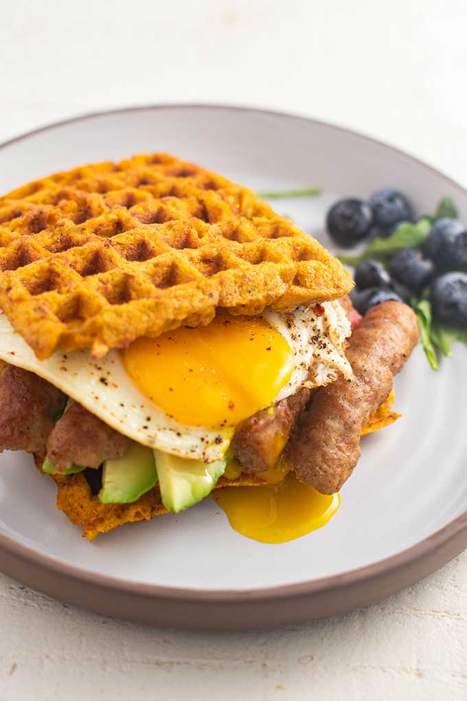 A sweet potato waffle breakfast sandwich with a broken egg yolk dripping out of the side.