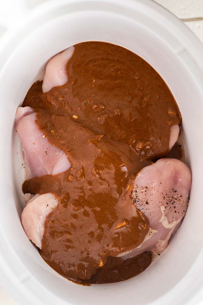 Chicken breasts covered in mole sauce in a crockpot.