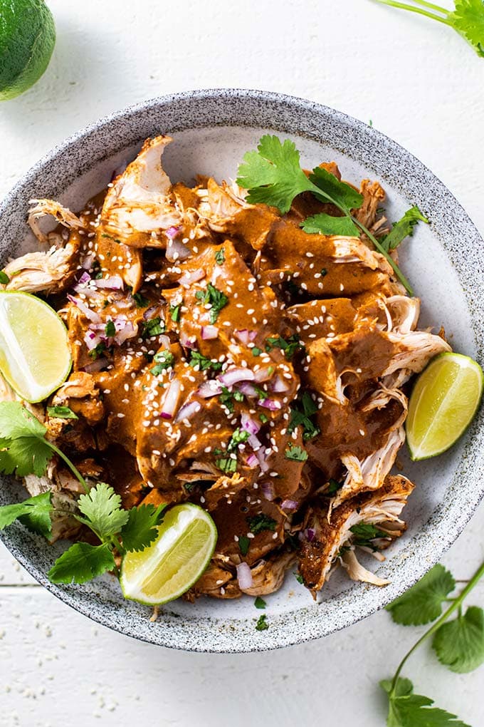 A bowl of shredded chicken with mole sauce, garnished with sesame seeds, cilantro and limes.