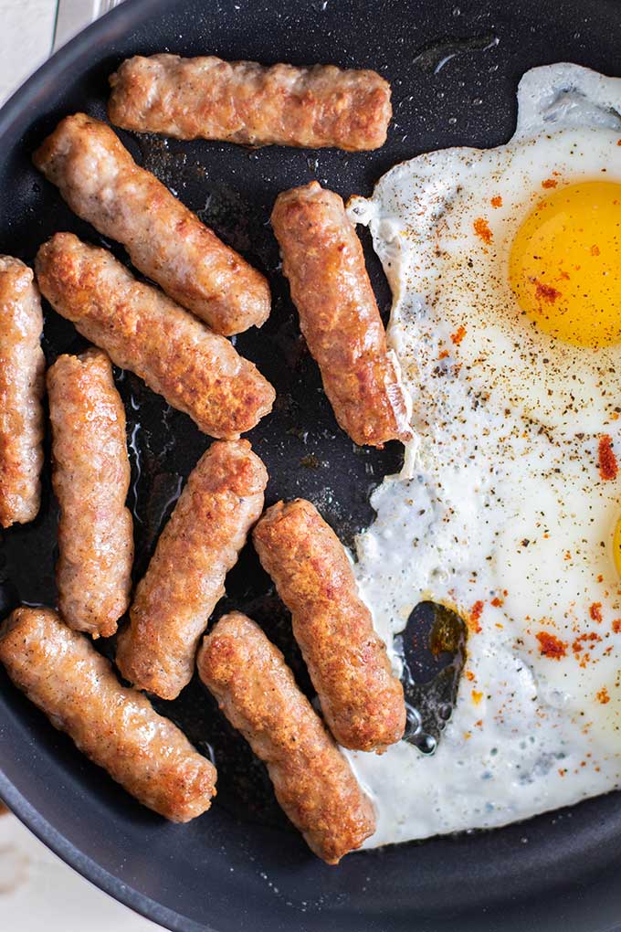 A frying pan with sausages and eggs cooking.