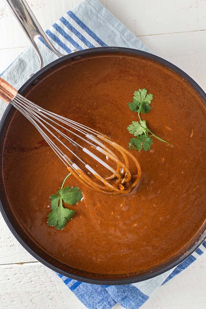 A large skillet with a whisk stirring a pot of mole sauce.