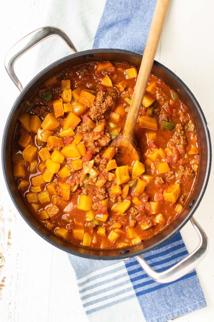 A top down view of a large pot of chili with big chunks of roasted butternut squash.