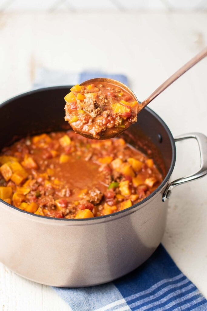 A ladle scooping chili out of a large pot.